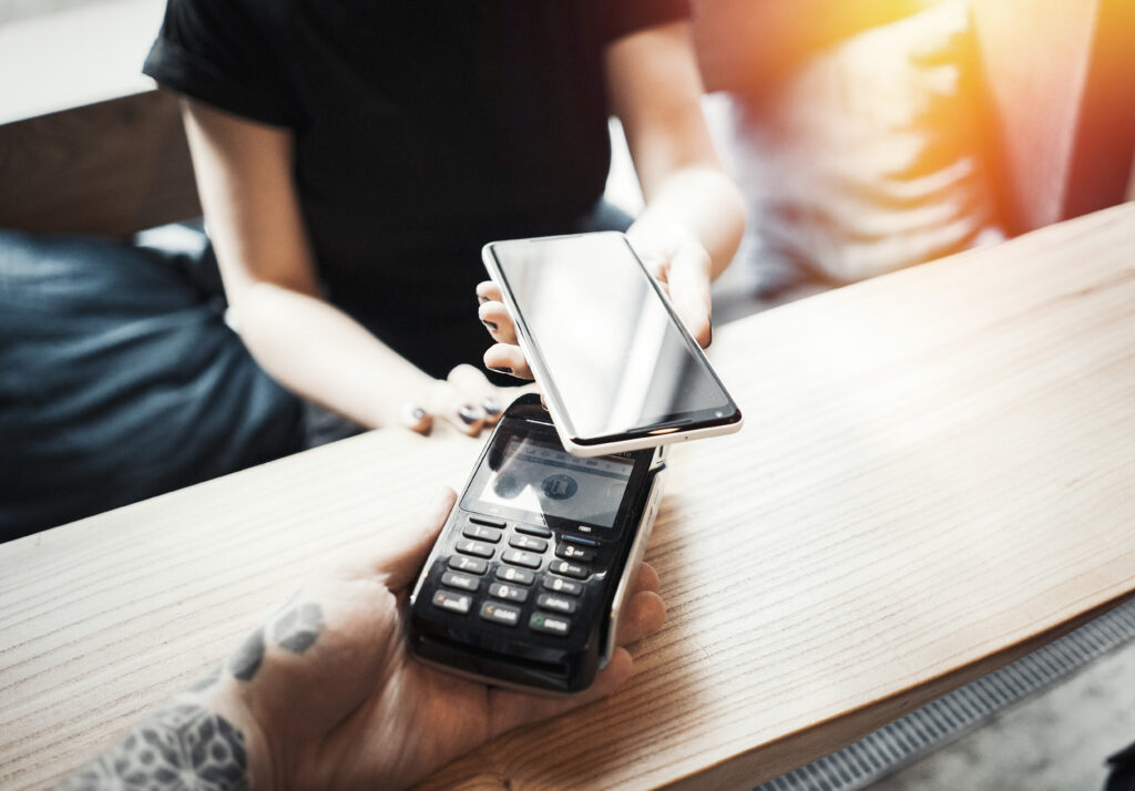 Young woman pays via payment terminal and mobile phone in cafe.